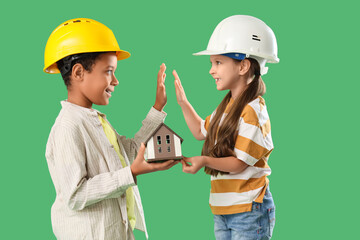 Canvas Print - Cute little architects with house model giving high-five to each other on green background