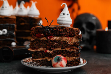 Poster - Piece of tasty Halloween cake with ghosts, eye and spider on black table against orange background