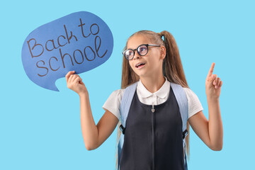 Wall Mural - Cute little girl in school uniform holding speech bubble with text BACK TO SCHOOL and pointing at up on blue background