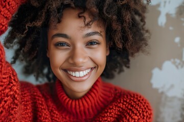 A young woman with curly hair smiles brightly, radiating joy as she enjoys a moment in a relaxed indoor environment.