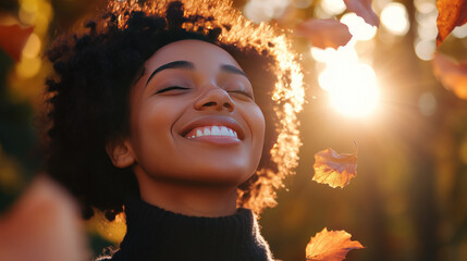 smiling black woman eyes closed with sun on her face wearing turtleneck in autumn park surrounded by falling leaves golden sunlight bokeh seasons changing fall outdoors face towards the sun