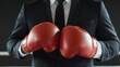 © Tonton54 - A businessman in a suit holds red boxing gloves, symbolizing determination and competition in the corporate world.