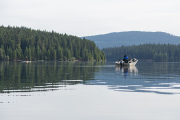 Old man solo fishing in a small boat in the middle of a forest lake with many different fishing rods. Old fisherman high quality picture for download