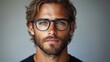 © Рудой Максим - Handsome man with glasses and tousled hair gazes confidently at the camera in a neutral background setting