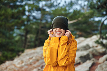 Canvas Print - Happy woman in stylish yellow raincoat enjoying a rainy day with hands to her face Fashionable Rainy Day Beauty Smile Travel Concept