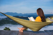 © Farknot Architect - Rear view of a woman reading book while sitting on hammock with mountain view and sea of fog