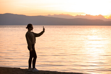 Wall Mural - Silhouette of a Woman Using a Smartphone at Sunset by the Lake