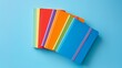 © Zhanna - A fanned-out arrangement of colorful notebooks on a bright blue background. The notebooks feature various solid colors, creating a vibrant and cheerful composition ideal for educational and creative