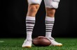 © Emqan - Close-up of football player's leg in striped socks on grass holding an American football