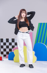 Wall Mural - Fashionable photo concept stylish young cool confident woman model Asian beautiful female wearing trendy black color knitted short jacket and white jeans, posing in a studio on a colorful background.