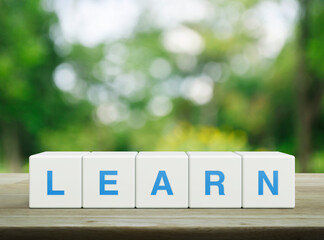 Poster - Learn letter on white block cubes on wooden table over blur green tree in park, Business, education and learning concept