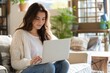 © Vadym - Young woman sits in armchair, using laptop on lap in modern home interior. Curly-haired female rests in casual attire, smiling at computer screen. Plaid background, sunny window adds comfort.