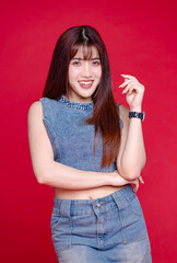 Fashionable photo concept stylish portrait young confident woman model Asian beautiful female wearing trendy denim sleeveless short top and jeans mini skirt, posing in studio on red background.