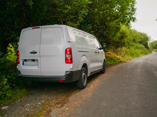 Wall Mural - A white medium size van is parked on a small county road in rural area with a red tail light. The road is empty and the sun is shining brightly. Product delivery to remote locations concept.
