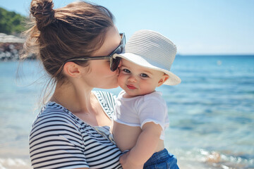 Wall Mural - a happy mother wearing sunglasses and a striped T-shirt, holding her son who is wearing a white hat, blue shorts