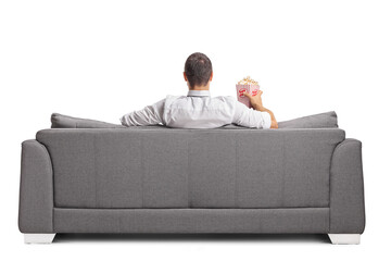 Rear view shot of a man sitting on a sofa and eating popcorn