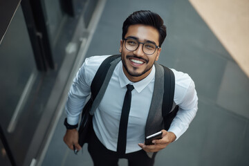 Poster - young stylish indian businessman walking happy holding a phone looking up