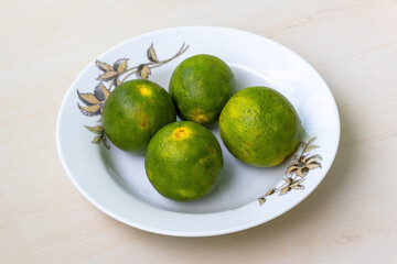 Fresh green malta fruits on a white plate on a light wooden surface.