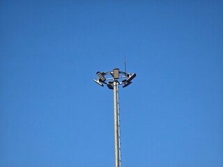 A tall metal streetlight with multiple lamps set against a clear blue sky. The minimalist composition highlights the modern urban infrastructure and clean background.