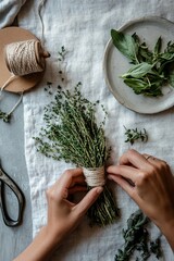 A close-up of hands wrapping fresh herbs with twine, with scissors and twine spool beside them