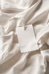 Poster - White fabric with crumpled texture features small silver tag on string. Close-up shot of laundry care label on white shirt material. Simple design highlights eco-friendly, minimalist fashion trends.