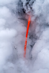 Wall Mural - Lava tube flowing into ocean in Hawaii at dawn shows the poisonous steam rising as the hot liquid hits the ocean.