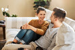 © Chanelle2000/peopleimages.com - Sofa, couple and conversation with smile for joke, funny memory and bonding together in marriage. Happy people, woman and man with love embrace for admiration, commitment and connection at home