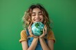 © chutikan - photograph of Joyful young woman holding Earth globe on green background for Earth Day