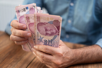 Poster - Male traveler holds Turkish lira banknotes in hands counting cash after exchange service of volatile currency with high inflation sitting at table in airport