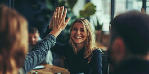 Wall Mural - A woman is smiling and giving a high five to another woman. The scene is set in a room with a table and chairs. There are other people in the room, but they are not the main focus of the image