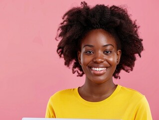 Wall Mural - A woman with curly hair is smiling and wearing a yellow shirt. She is holding a laptop in her hand