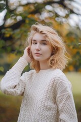 Wall Mural - A blonde woman is standing in a field with a white sweater on. She is looking at the camera with a smile on her face