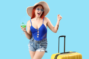 Wall Mural - Happy female tourist with cocktail and suitcase on blue background