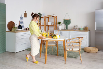 Wall Mural - Young woman holding tray with lemonade and lemons in kitchen