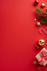 Wall Mural - Celebratory Christmas vertical background featuring colorful ornaments, a wrapped gift, and green fir branches on a vibrant red backdrop evoking holiday spirit and joy