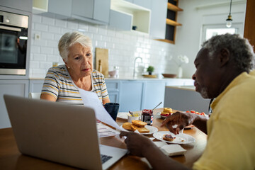 Wall Mural - Diverse senior couple going over financials with laptop during breakfast