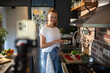 © Geber86 - Smiling young woman cooking and filming with smartphone in modern kitchen