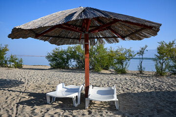 Two empty sunbeds are standing on a sandy beach under a beach umbrella