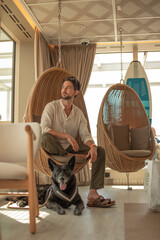 Young man sitting on a hanging chair during a trip with his dog by his side