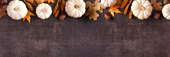 Poster - Fall top border of white pumpkins with muted orange and brown autumn decor. Above view on a rustic dark stone banner background with copy space.