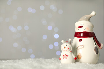 Wall Mural - Cute decorative snowmen on artificial snow against blurred lights. Space for text