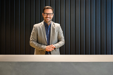 Wall Mural - portrait of confident male receptionist in eyeglasses looking at camera and standing at lobby desk