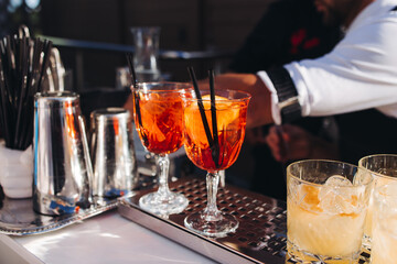 Wall Mural - Bartender working, beautiful row line of different coloured liquor alcohol cocktails on a open air party in a bar, and others on catering banquet on event, barman mixing drinks and beverages in club