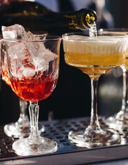 Wall Mural - Bartender working, beautiful row line of different coloured liquor alcohol cocktails on a open air party in a bar, and others on catering banquet on event, barman mixing drinks and beverages in club