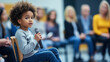 © AndyGordon - A child sitting in a chair during a town hall meeting, holding the microphone and expressing their views to a panel of adults