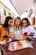 © Xavier Lorenzo - Vertical shot of three young women using mobile phone while enjoying aperitif in a bar. Millennial diverse italian girls chatting on smart phone while drinking red wine