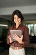 © insta_photos - Happy busy female professional executive using tab standing in office. Smiling young adult Hispanic businesswoman leader or entrepreneur, company worker using tablet at work. Vertical photo.