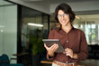 © insta_photos - Smiling young Hispanic professional business woman wearing glasses using tablet standing in office. Happy businesswoman company manager, female entrepreneur or employee looking at camera. Portrait.