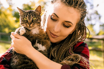 Young woman holding tabby cat outdoors in summer