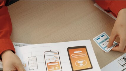 Startup company employee planning for user interface prototype for mobile application or website in office with model of program on desk. UX UI designer consider user friendly interface plan. Synergic